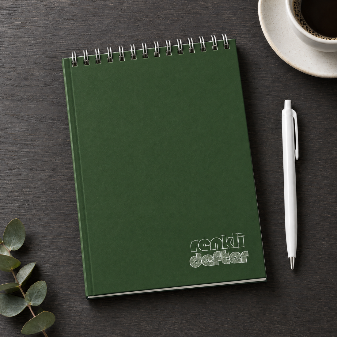 Yeşil defter A5 üstten spiralli sert kapak, beyaz kalem hediyeli, antrasit masa üzerinde